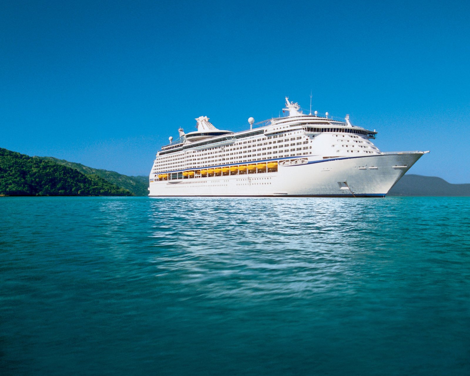 Adventure of the Seas au mouillage devant une côte verdoyante, coque blanche et mer turquoise