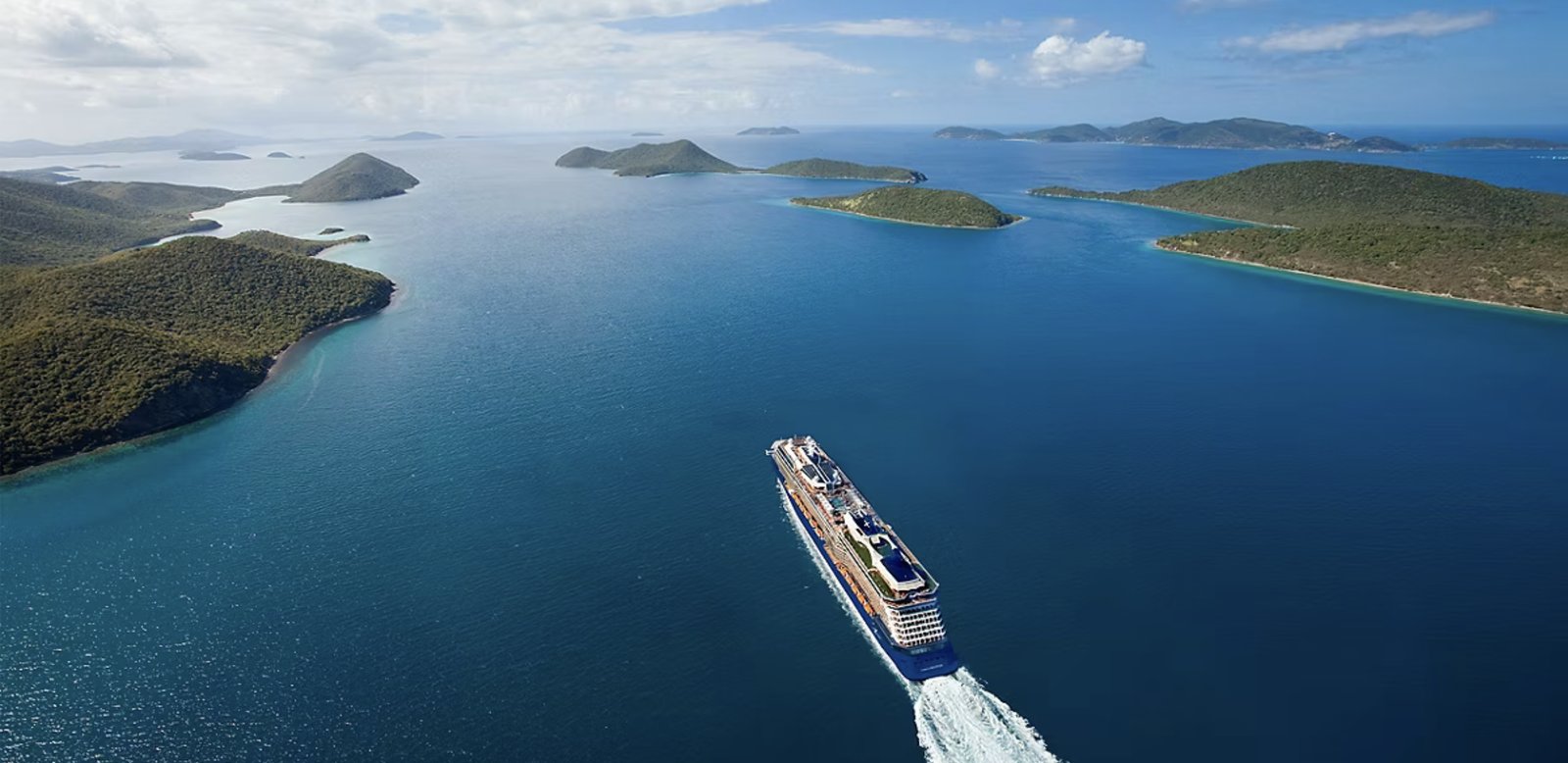 Vue aérienne du Celebrity Eclipse, coque bleu foncé, naviguant entre des îles verdoyantes, sillage visible à l'arrière